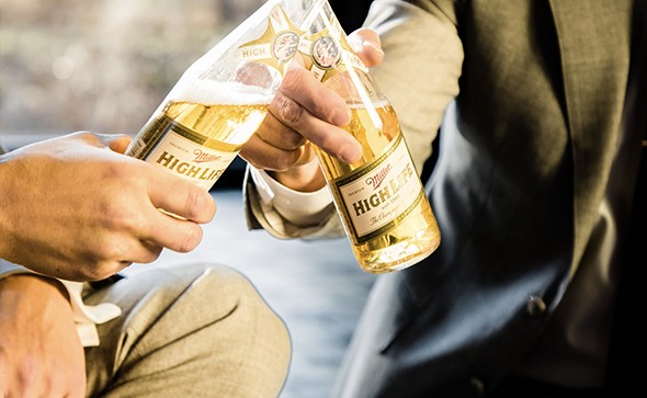 Image of two men clinking together two bottles of Miller High Life